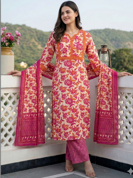 A woman models a traditional Indian salwar kameez suit set featuring a floral print. The kurta has a cream base with vibrant pink and orange floral patterns, paired with matching pink trousers and a dupatta with a solid pink border.