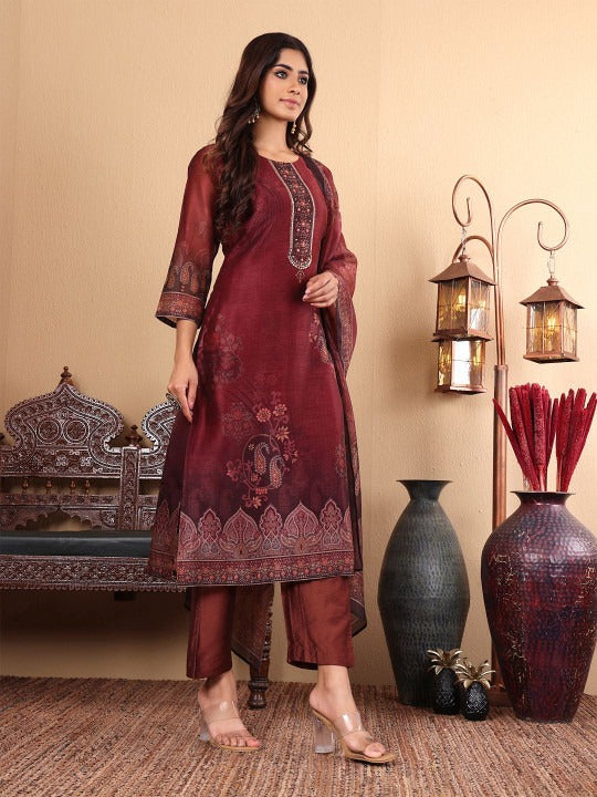 Woman in a maroon traditional outfit standing in a room with decorative vases and lamps.